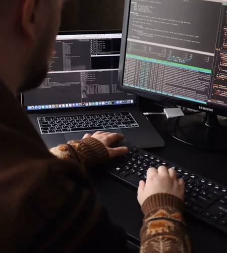 A developer at two screens filled with terminal output and logs.